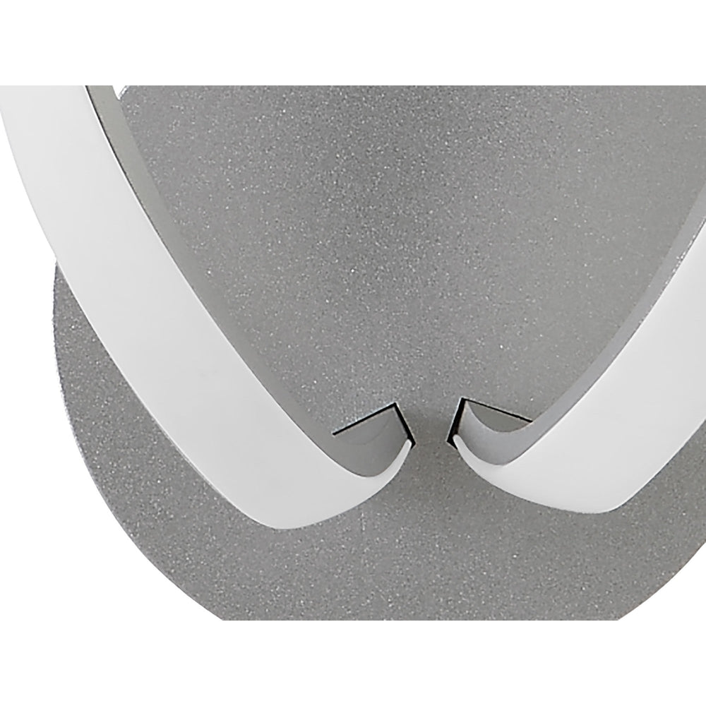 Close-up of the Knot LED wall light showing the polished chrome looped frame meeting a frosted white diffuser against a silver textured backplate.