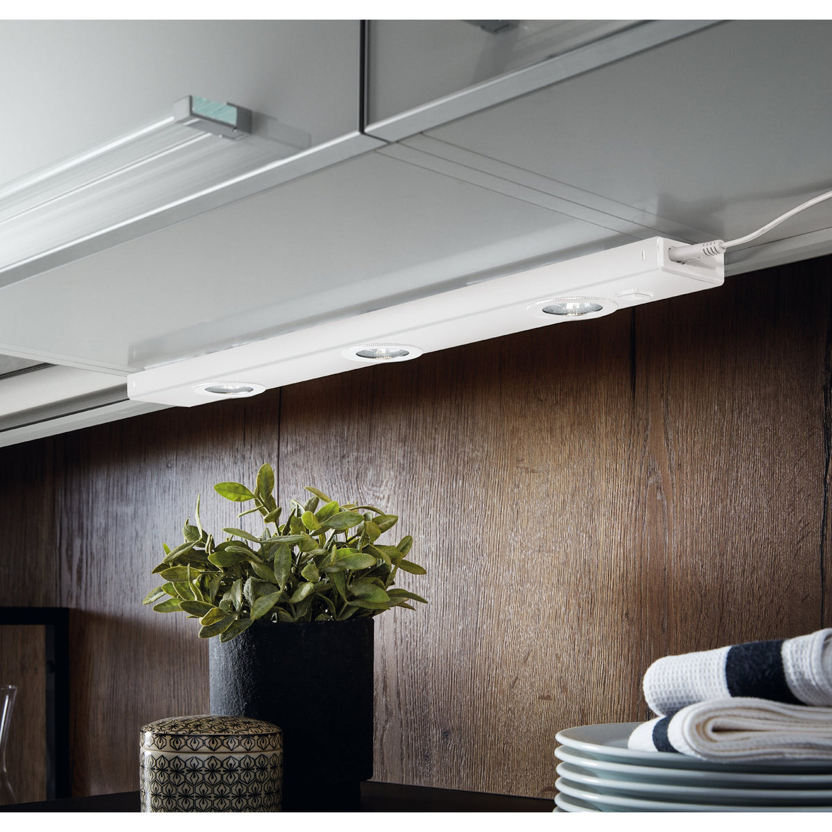 Kob Under Cabinet Light in white steel, a slim bar with three round integrated LED spotlights, shown mounted beneath a kitchen cabinet above a wooden worktop.
