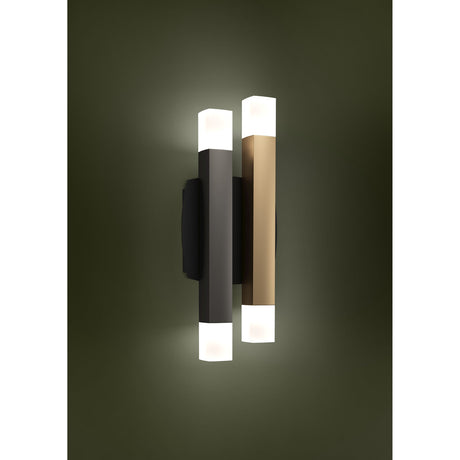 Korbelle LED wall light with two offset square bars, one grey and one brown, on a black backplate, each with frosted top and bottom diffusers glowing warm white against a dark green wall.