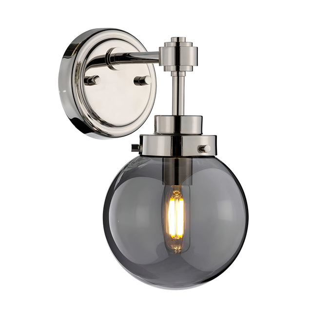 The Kula 1 Light Wall Light in Polished Nickel features a modern design with a semi-transparent mirror glass shade and a glowing filament bulb, all mounted on a circular base.