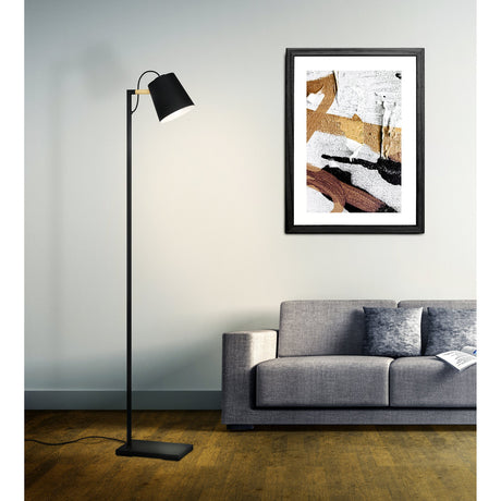 Lacey Floor Lamp in black and brown, slim steel stem with rectangular base and wood-accented arm holding a tapered black shade, shown beside a grey sofa in a living room.