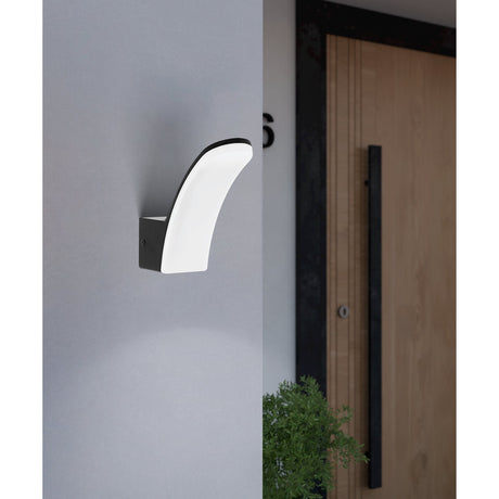 Laconella-E LED outdoor wall light with curved white plastic diffuser on a black square mount, fitted beside a wooden front door on a grey exterior wall.