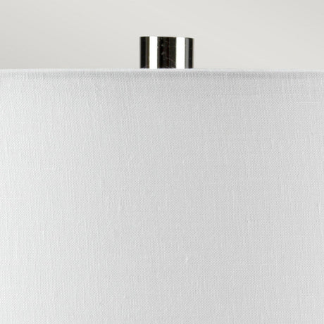 Close-up of the top portion of a white fabric lampshade with a small shiny metallic finial on top, enhancing the sleek design of the Laguna 1 Light Small Table Lamp in Turquoise & Graphite Glaze, set against a plain light gray background.