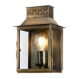 The Lambeth Palace 1 Light Outdoor Wall Light - Aged Brass boasts a glass enclosure with a visible glowing bulb, radiating vintage charm. Its aged brass finish and ornate cut-out patterns on the top enhance elegance in any outdoor environment.