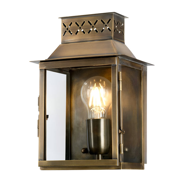 The Lambeth Palace 1 Light Outdoor Wall Light - Aged Brass boasts a glass enclosure with a visible glowing bulb, radiating vintage charm. Its aged brass finish and ornate cut-out patterns on the top enhance elegance in any outdoor environment.