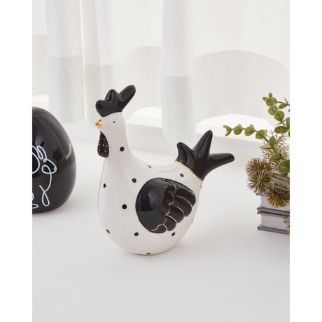 Landjut ceramic cockerel ornament with a white polka-dot body, black comb, wings and fanned tail, and gold beak detailing, displayed on a table beside a black egg ornament and greenery.