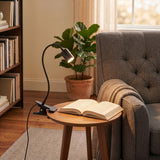 Lardaro Clamp Lamp in black with a flexible gooseneck arm and cylindrical head, clipped to a side table and illuminating an open book beside an armchair.