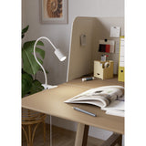 Lardaro Clamp Lamp in white, clipped to a desk edge with a flexible gooseneck arm and cylindrical spotlight head, shown in a study setting with a magazine and desk accessories.