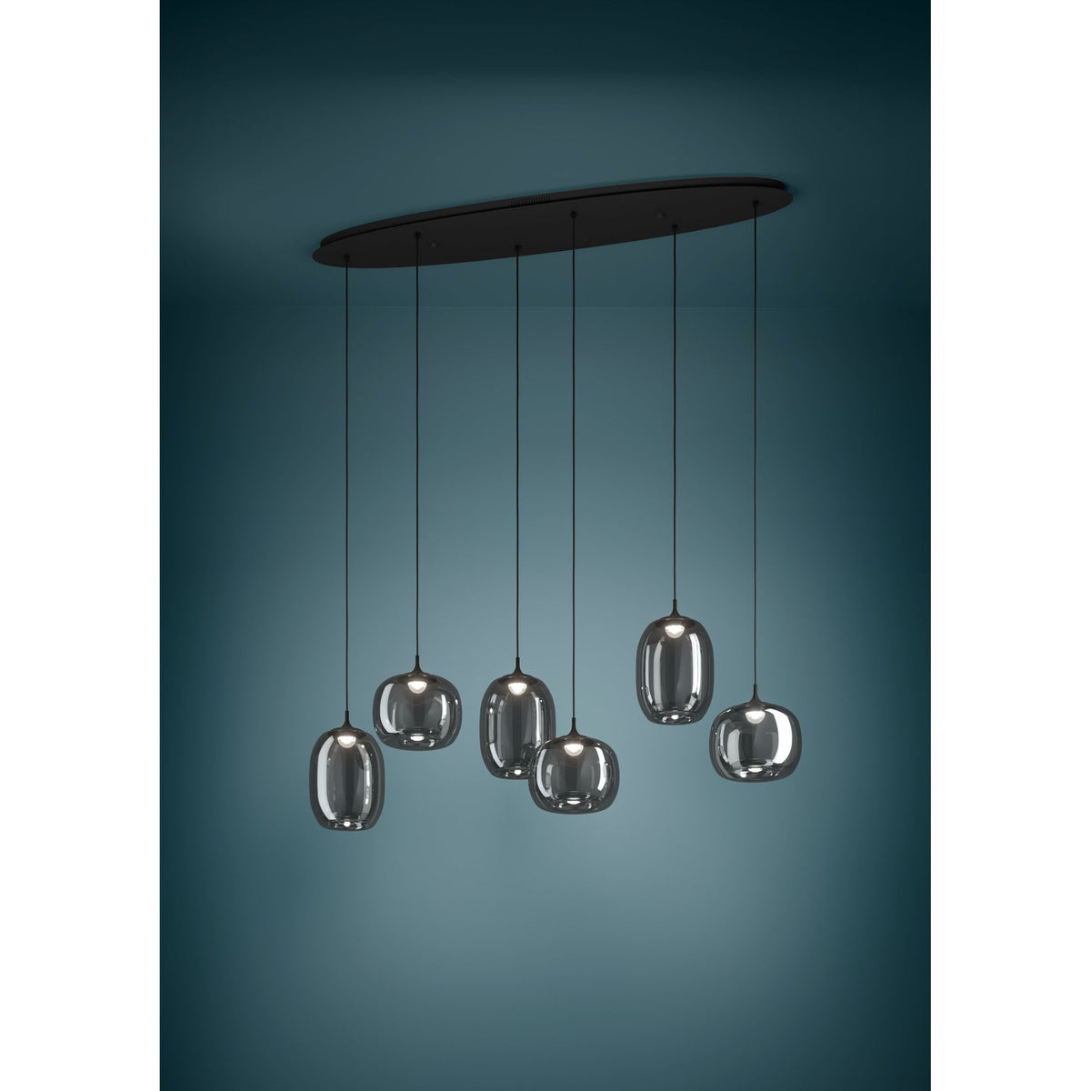 Black Larva linear pendant light with six staggered smoked glass barrel and globe shades on a long oval ceiling plate, shown against a dark teal background.