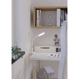 Lauro Clamp Lamp in white, shown clamped to a desk edge with its round LED head on a flexible gooseneck, illuminating a study desk beside books and a shelf.