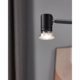 GU10 LED spotlight bulb with faceted glass reflector fitted in a matte black adjustable wall light, glowing cool white against a grey interior wall.