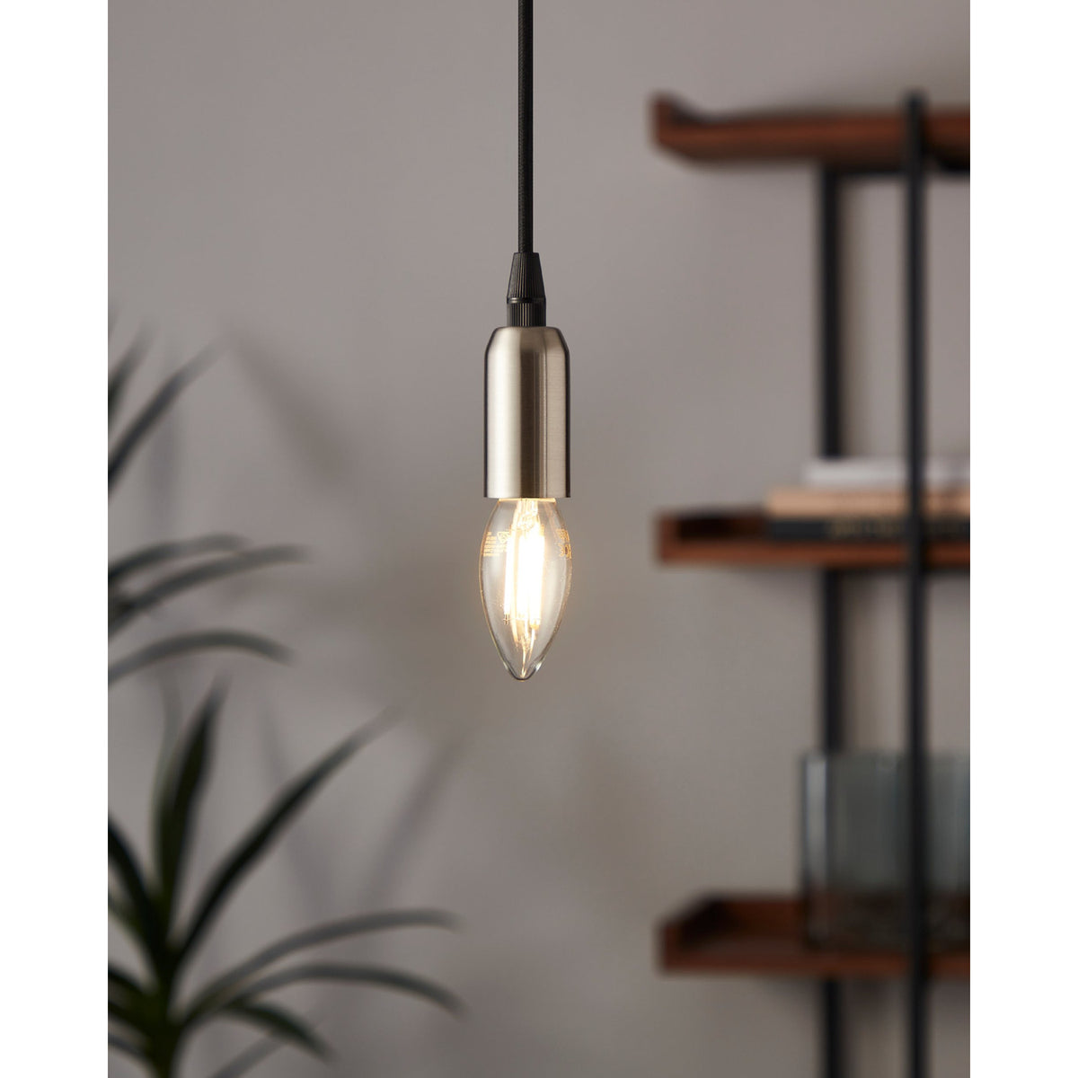 Pendant light with brushed nickel fitting and black cord holding an LED candle bulb E14 C35, lit warm white, shown in a room beside wooden shelving and a plant.