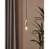 Pendant light fitted with a G9 LED capsule bulb, brass holder and blue cable, glowing warm against a muted pink wall with curtain and plant nearby.
