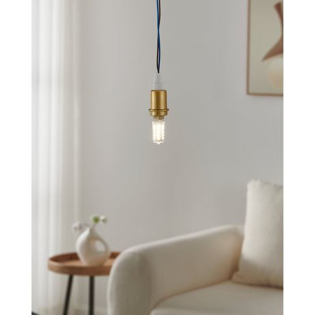 LED capsule bulb with G9 cap and brass pendant fitting, lit in a living room setting with sofa, side table and curtains in the background.