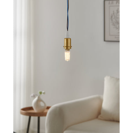 Lit G9 LED capsule bulb in a brass pendant fitting hanging above a cream sofa, showing warm white light from the clear capsule with visible LED chips.