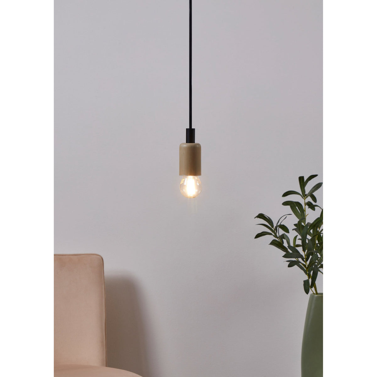 Pendant light with wood-effect holder and black cord fitted with an LED golf ball bulb, E27 glass globe glowing warm white, shown above a beige sofa near a green plant.