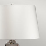 The Lena 2 Light Large Plum Table Lamp with an off-white shade and metallic base is set against a neutral gray background, showcasing its sleek, minimalist design. The use of mouth-blown glass enhances its modern aesthetic, even when the lamp is turned off.