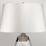 The Lena 2 Light Small Blue Table Lamp showcases an off-white fabric shade paired with a textured, mouth-blown glass base. It is accentuated by a polished metal detail connecting the base to the shade, all highlighted against a neutral gray backdrop.
