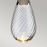 A close-up of the Lena 2 Light Small Blue Table Lamp featuring an off-white shade. The dual-lit system casts a warm glow, highlighting the intricate patterns. The lamp stands against a neutral gray background.