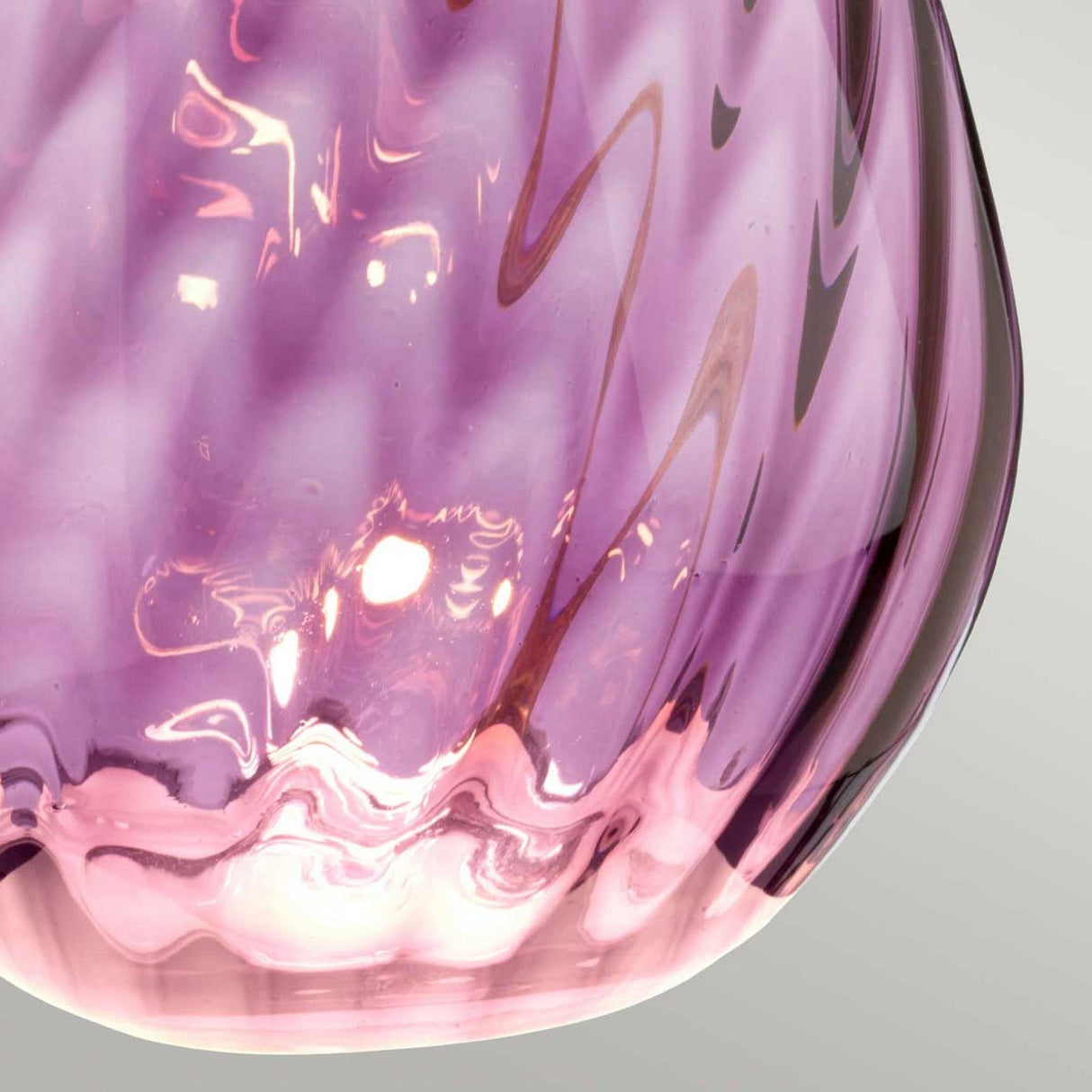 Focused view of a Lena 2 Light Small Plum Table Lamp featuring a decorative glass design with a swirl pattern and translucent texture. Light reflects off its surface, creating off-white hues on the soft, rippled features. The background is a simple light gray.