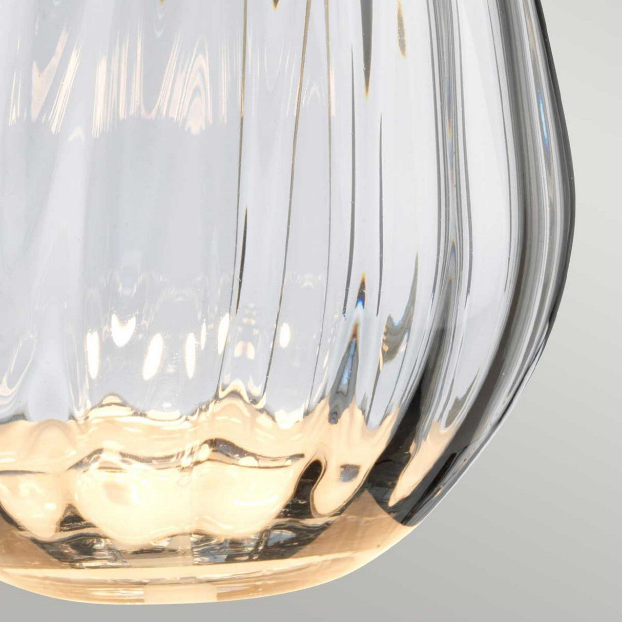 A close-up of a smoke-tinted glass object, emitting a warm golden glow, is set against a light gray background. The intricate texture creates a shimmering effect that evokes the elegant design of the Lena 2 Light Small Smoke Table Lamp with a Slate Shade.