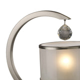 A close-up of the Lincoln 1 Light Crystal Table Lamp featuring a curved satin nickel arm, a cylindrical frosted glass shade, and a crystal teardrop ornament above the illuminated light.