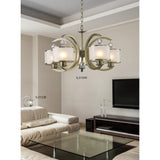 Modern living room with a beige sectional, glass coffee table, and a contemporary chandelier. The Lincoln 1 Light Crystal Table Lamp—satin nickel with glass shade—adds elegance atop the side table.
