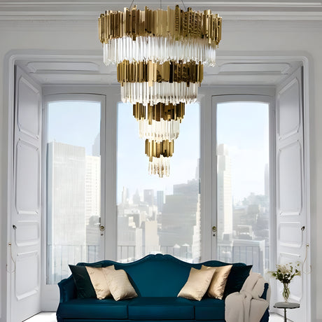 A luxurious living room featuring a Royal 30/53 Light Crystal Chandelier in Gold with cascading tiers of crystal, complemented by a teal velvet sofa. Large windows offer a stunning cityscape view, while the white walls and ornate molding enhance the sophisticated atmosphere.