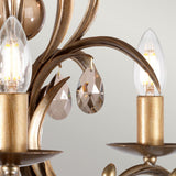 Here's a rewritten version using the provided product data:

A close-up of the Lily 5 Light Chandelier - Bronze Patina reveals its elegant bronze finish, showcasing candle-shaped LED bulbs and smoked cut glass droplets that resemble teardrop-shaped crystals, gracefully hanging from decorative metal curves against a light background.