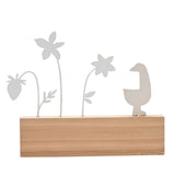 Metal wall plaque with a white goose silhouette beside cut-out flower stems in white and grey, mounted on a brown wooden base, shown against a plain white background.