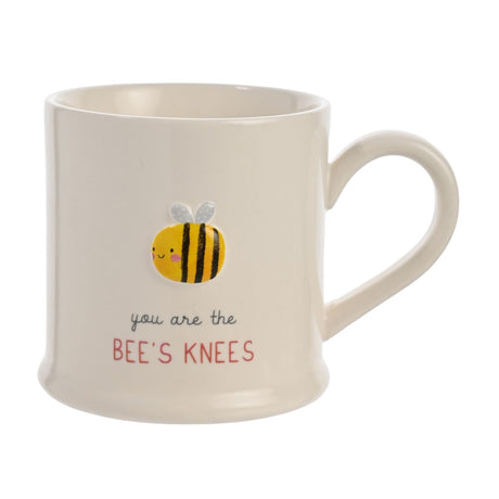 White stoneware mug with embossed smiling bee design and text "you are the BEE'S KNEES" in black and red, shown on a plain white background.