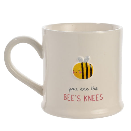 White stoneware mug with looped handle, featuring an embossed smiling bee design and the text "you are the BEE'S KNEES" on a plain background.