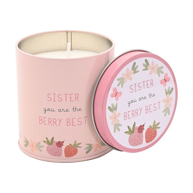 Pink round tin scented candle, 8cm x 8cm, reading "Sister you are the Berry Best" with strawberry, ladybird and floral illustrations, lid propped beside the lit wick, on a white background.