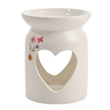 White ceramic wax melt burner with a round base, heart cutout, wide top dish, and painted pink flowers and butterfly, set against a plain background.