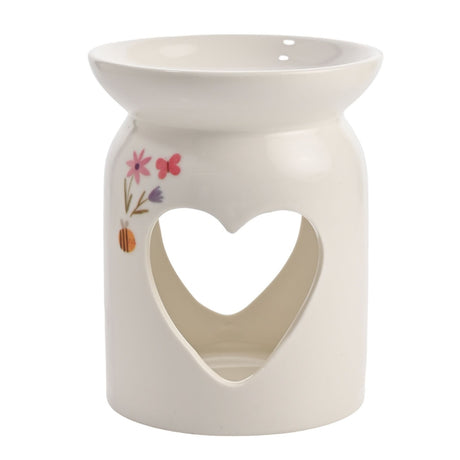 White ceramic wax melt burner with a round base, heart cutout, wide top dish, and painted pink flowers and butterfly, set against a plain background.