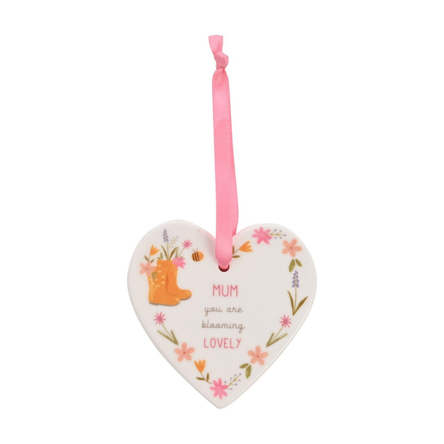 White ceramic heart-shaped wall decoration with pink ribbon, printed with "MUM you are blooming LOVELY" surrounded by floral designs and orange wellington boots.
