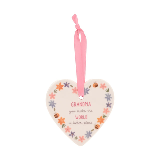 White ceramic heart hanging decoration with floral border and "Grandma, you make the world a better place" text, pink ribbon, plain background.