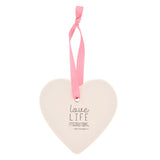 White ceramic heart hanging decoration with pink ribbon, shown reverse side printed with "Love Life Celebrations" text, on a plain white background.