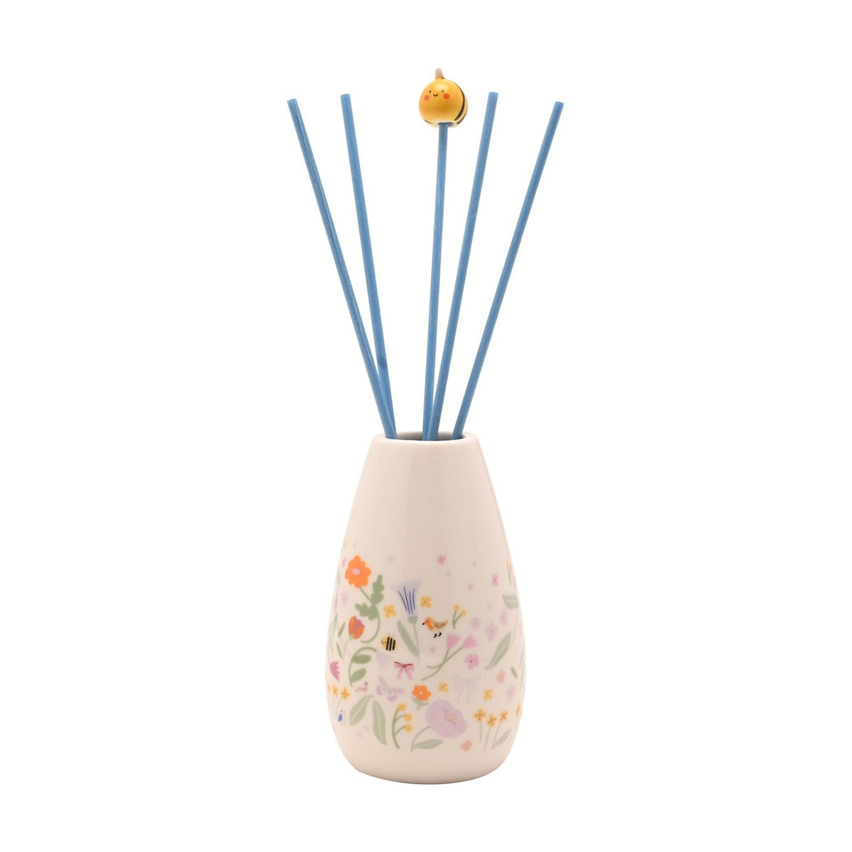 Ceramic reed diffuser in a cream tapering vase with a floral meadow print of flowers, bees and a small bird, blue reeds topped with a yellow chick bead, on a plain white background.
