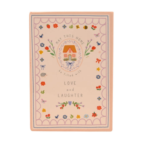 Peach stoneware book vase shaped like a storybook, featuring a cottage design, floral and bird motifs, and "Love and Laughter" text, set against a plain white background.