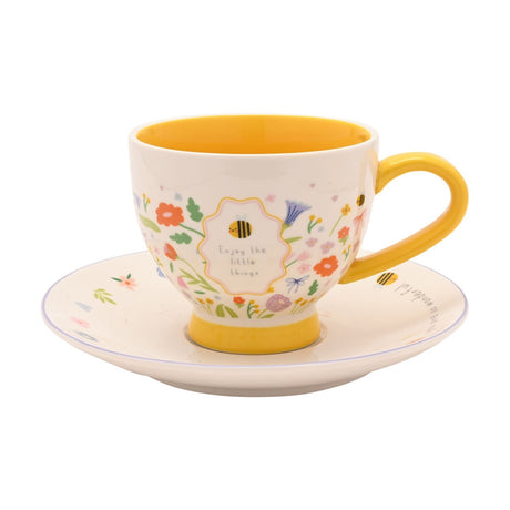 Little Things Stoneware Cup & Saucer in off white with a yellow interior and handle, decorated with small florals, bees and the words "Enjoy the little things", on a plain white background.