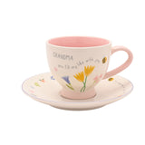 Stoneware cup and saucer with "GRANDMA you fill my life with joy" text, pink interior and handle, floral tulip design, on a plain white background.