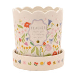 White stoneware planter with scalloped rim and matching saucer, decorated with a floral meadow print, bees and bows, reading "TEACHER thank you for helping me grow" on a plain background.