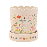 White stoneware planter with scalloped rim and matching saucer, decorated with a floral meadow print of flowers, leaves, bows and bees, shown on a plain white background.