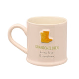 Cream stoneware mug with embossed yellow and orange welly boots above "GRANDCHILDREN bring love & sunshine" text, shown on a plain white background.