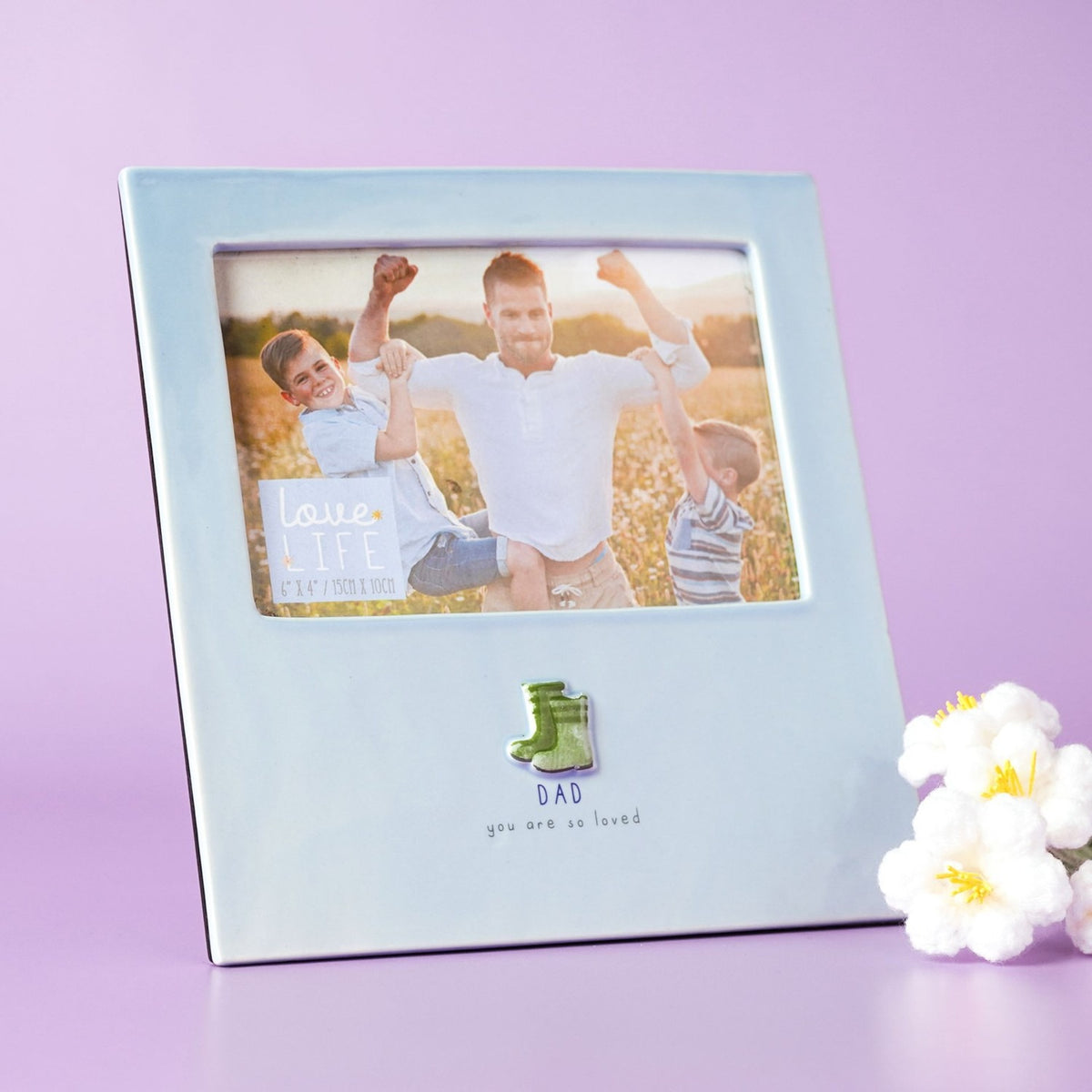 Blue glazed stoneware photo frame with raised green welly boots and "DAD you are so loved" text, holding a 6 x 4in landscape photo, shown on a purple background.