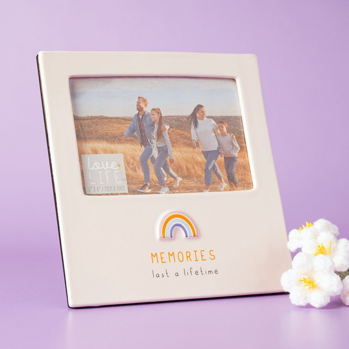 Cream glazed stoneware photo frame with rectangular 6 x 4in landscape window, raised pastel rainbow and "MEMORIES last a lifetime" text, set against a lilac background.