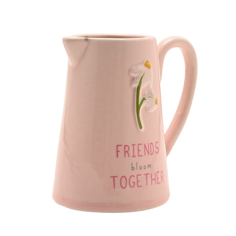 Pink stoneware jug with glossy finish, featuring embossed white flowers on a green stem and "FRIENDS bloom TOGETHER" text, set against a plain white background.