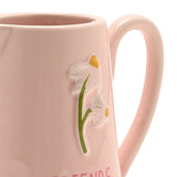 Close-up of a pink stoneware jug with a glossy finish, showing an embossed white flower design with yellow centres on a green stem above "Friends" text.