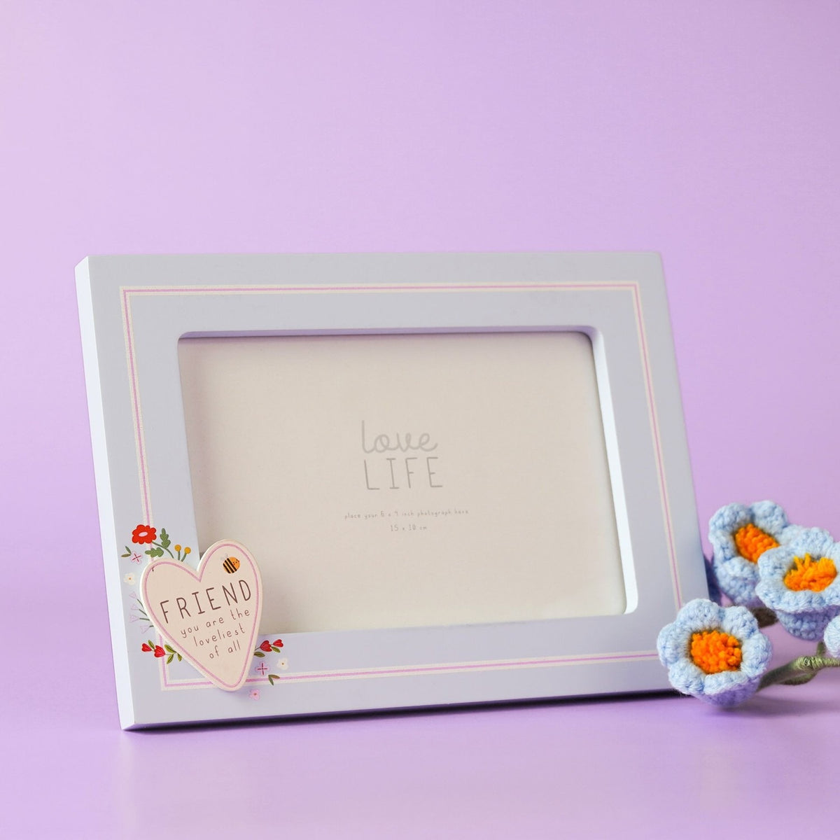 Blue wooden rectangular photo frame with stand, featuring a cream heart reading "FRIEND you are the loveliest of all" with floral details, shown against a lilac background.
